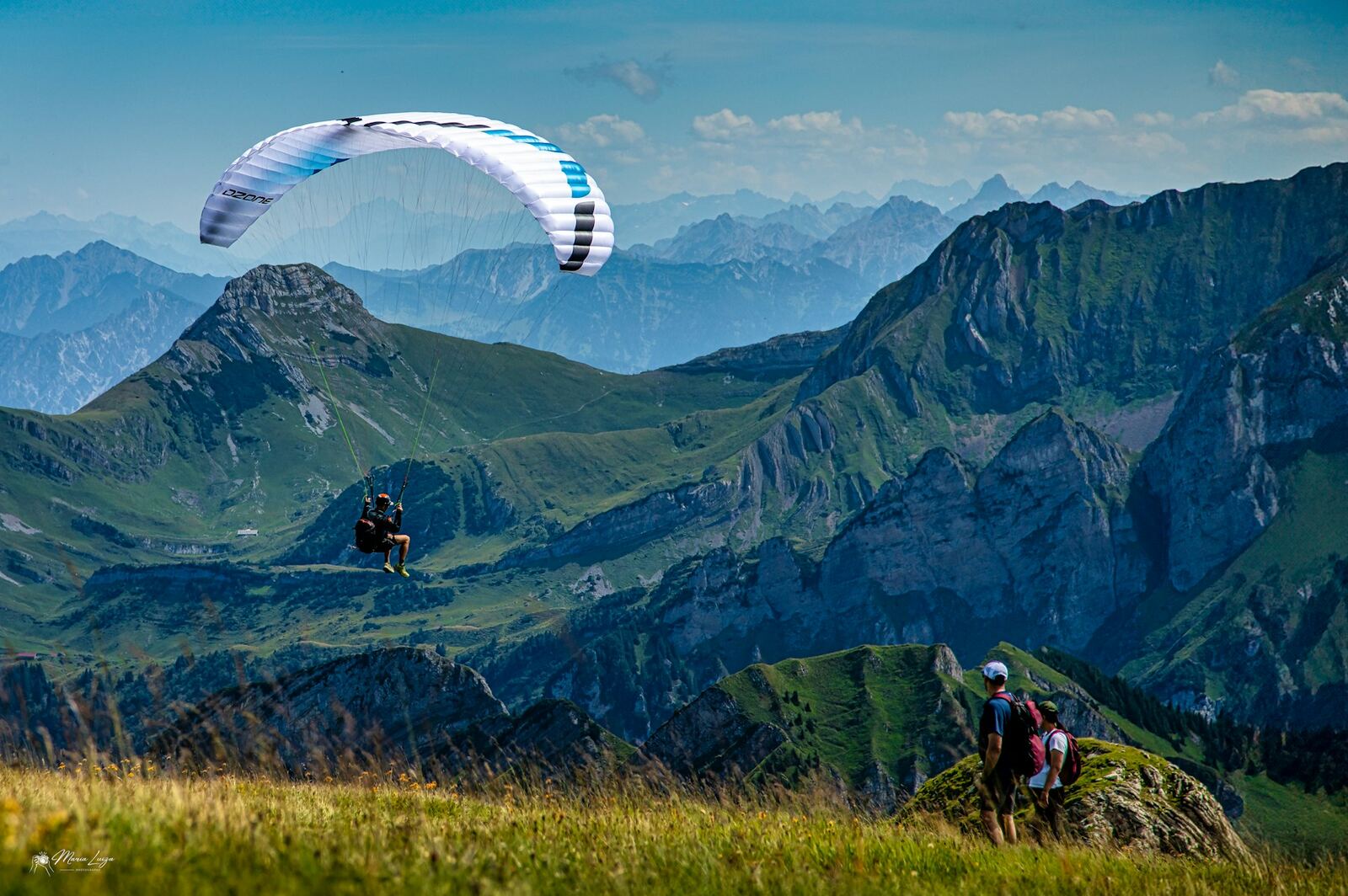 Paraglider flying over green mountains