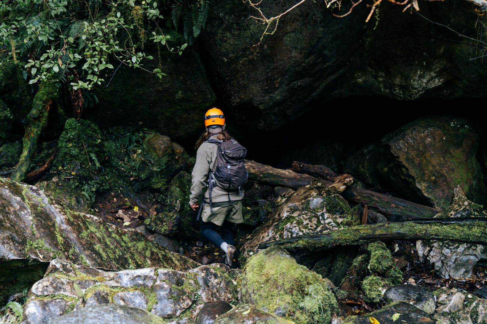 Person in a helmet at a mossy cave entrance