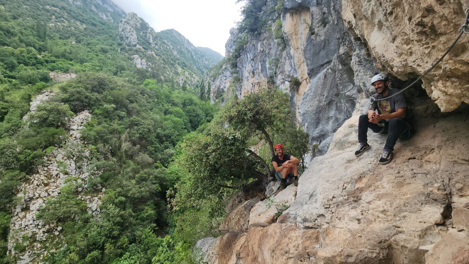 Two people on a rock wall above a green gorge